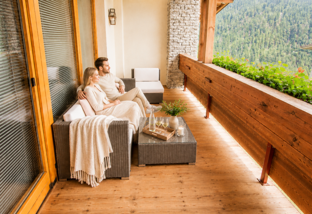Paar entspannt auf der Terrasse eines Luxus-Apartments mit Blick auf bewaldete Berge in Österreich